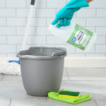 Hand wearing a teal glove pouring Great Value cleaning vinegar into a gray bucket with mop and sponge nearby.
