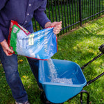 Person pouring granular GreenView Fall Lawn Food from a bag into a blue lawn spreader on a grassy yard