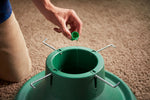 Close view of hands pouring liquid from a small green cap into the reservoir of a green tree stand.