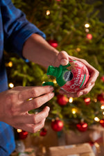 Liquid being poured from a Miracle-Gro Christmas Trees bottle into a small green cap with a decorated tree in background.