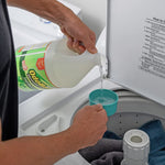 Hands pouring OdoBan disinfectant concentrate into a measuring scoop above an open top-load washing machine