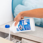 Hand pouring OUT White Brite laundry whitener powder from bottle into washing machine dispenser next to a laundry hamper
