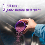 Hand pouring purple fragrance crystals from a filled purple cap into a washing machine drum with usage instruction text overhead.