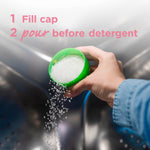 Hand pouring white scent booster crystals from a green cap into a washing machine drum with instructional text