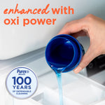 Close-up of a hand pouring bright blue liquid from a measuring cap into a washing machine drawer with Purex 100 years badge.