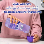 Person pouring white Snuggle booster beads from a purple bottle into a measuring cup with text about 95% naturally derived ingredients.