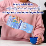 Person pouring blue Snuggle scent booster granules from a bottle into a measuring cup with overlay text about naturally derived ingredients.