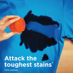 Hand pouring product from an orange cap onto a blue shirt showing a dark liquid stain and text 'Attack the toughest stains'