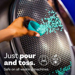 Hand pouring teal scent booster beads into a washing machine drum with text 'Just pour and toss'