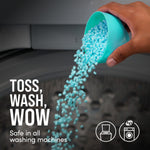 Hand pouring blue-green scent beads from a scoop into a washing machine with text "TOSS, WASH, WOW"