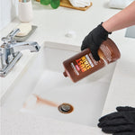 Hand wearing black glove pouring Whink Rust Stain Remover into a white sink to treat rust stain