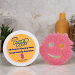 Scrub Daddy PowerPaste tub and pink Scrub Mommy sponge displayed on a kitchen countertop with decorative background