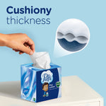Hand pulling a tissue from a Puffs cube box with inset graphic showing cushiony thickness and a magnified cross-section