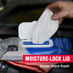 Hand pulling a white wipe from an STP pack through a moisture‑lock lid on top of a folded red cloth, product text overlay visible