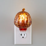 Tortoiseshell pumpkin fragrance warmer plugged into an outlet, illuminated and glowing