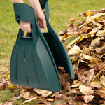 Close-up of two dark green interlocking leaf scoops held over a pile of dry leaves on grass.