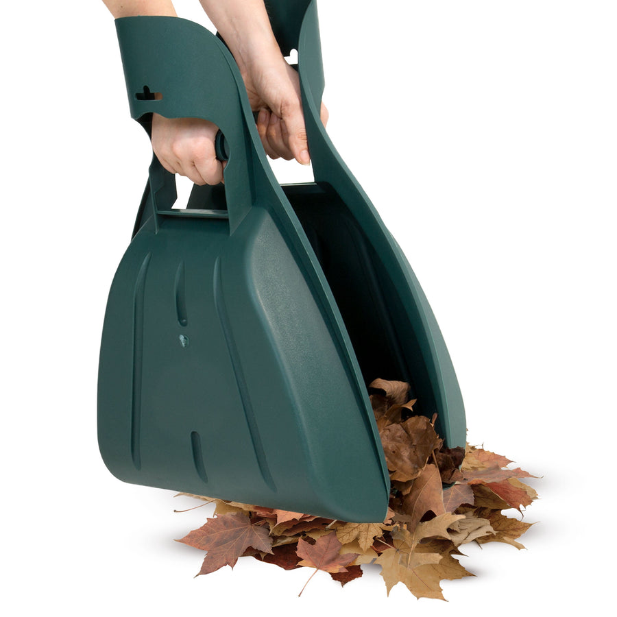 Pair of dark green plastic leaf scoops being held together to pick up a pile of dry leaves.