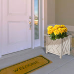 White lattice planter placed by a front door filled with yellow chrysanthemums on a porch