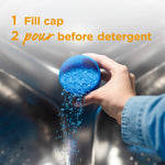 Hand pouring blue fragrance crystals from a filled cap into a washing machine with usage instructions text