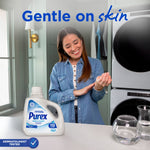Woman in laundry room smiling while rubbing her wrist, Purex Free & Clear detergent jug visible on counter and ‘Gentle on skin’ text