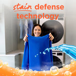 Woman holding up a bright blue shirt in a laundry room with 'stain defense technology' headline and splash graphics