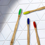 Four Pursonic bamboo toothbrushes with colorful bristles arranged on white geometric tiled surface in a lifestyle layout
