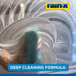Hand wiping sudsy cleaner across glass in circular motions with Rain‑X logo and caption promoting deep cleaning formula.