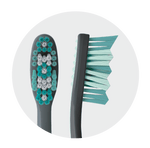 Circular close-up of a toothbrush head and side profile showing multi-level teal and white bristles against a light background.