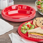 Stack of red compartment plates on a table with a plated sandwich, salad and cookies shown on one plate