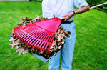 Person holding a red leaf rake loaded with dried leaves captured over a black dust pan on green lawn