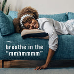 Woman smiling and lying on a teal sofa above text 'breathe in the "mmhmmmm"', lifestyle image implying freshness.
