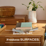 Wood tabletop scene with books and vase and overlaid text stating 'Removes DIRT. Freshens SURFACES.'
