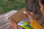 Hands holding a cardboard support panel and peeling a small adhesive tab from a FlyPad trap backing