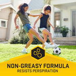 Two children playing soccer on a lawn with a yellow banner reading “Non-Greasy Formula Resists Perspiration.”