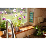 FlyPad sticky trap mounted vertically on a kitchen tile wall next to a window with potted flowers on the sill