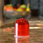 Red translucent dome-style fruit fly trap sitting on a kitchen counter with blurred fruit bowl in background