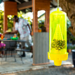 Close-up of a hanging translucent yellow RESCUE! trap filled with trapped insects, blurred backyard gathering in background.