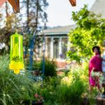 Translucent neon-yellow RESCUE! yellowjacket trap hanging in a lush garden with a blurred couple in the background.