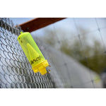 Angled shot of a translucent yellow RESCUE! trap hanging on chain-link fence with insects visible inside and flying below.