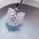 Close-up of white bristle head of a grey toilet brush inside ceramic toilet bowl with soapy water