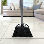 Front view of a Reynera angled broom head standing on a tiled floor with a sofa and cushions in the background.