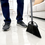 Reynera angled broom in a living room scene with a person standing nearby, showing bristles and gray handle.
