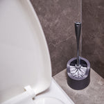 Grey toilet brush resting in matching caddy positioned beside a toilet on tiled floor