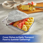 Rectangular dish of cut fruit partly covered with embossed foil showing a fireworks design on a cutting board