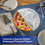 Lattice-top pie partially covered with embossed fireworks-pattern foil on a blue placemat beside serving utensils