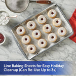 Baking sheet lined with Reynolds Kitchens parchment topped with jam-filled powdered cookies and baking tools nearby