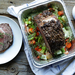 Roast beef on a bed of vegetables inside a Reynolds aluminum roasting pan on a rustic wooden surface