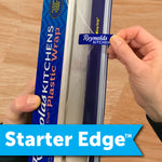 Close-up of hands using the starter edge pull tab on a Reynolds Kitchens plastic wrap box showing the brand label