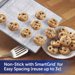 Baking sheet lined with Reynolds Kitchens parchment paper with SmartGrid pattern and a plate of chocolate chip cookies