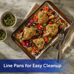 Baking sheet lined with Reynolds parchment under roasted chicken and vegetables, styled on marble with herbs.
